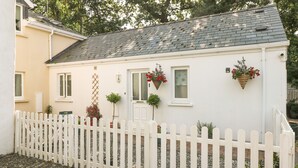 A white house with a white picket fence, a gravel driveway, and potted plants. - Love Cottage (Tenby)