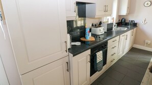 A compact kitchen with white cabinets, a black countertop, and a stove. - Love Cottage (Tenby)
