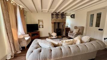 Een woonkamer met een bank, een televisie, een open haard en een klok aan de muur.