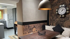 Una cuina moderna amb zona de menjador, que inclou una taula de fusta, una làmpada penjant i un rellotge de paret.