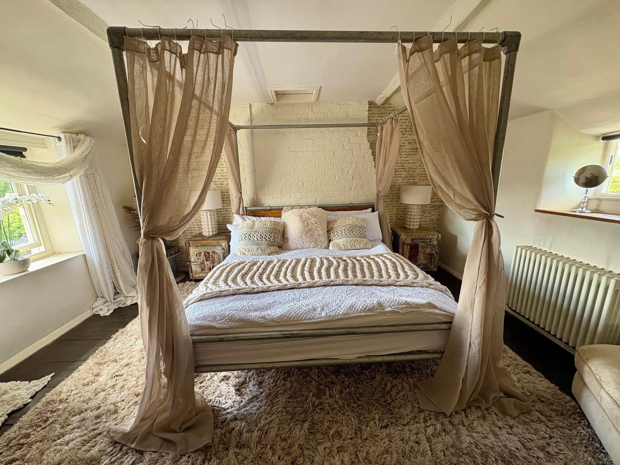 A four-poster canopy bed with a fluffy rug, bedside lamps, and a window with curtains.