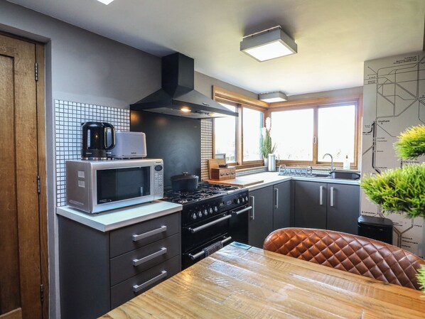 A modern kitchen with a microwave, stove, and kettle, featuring a large window and a map on the wall. - Coupling Cottage (Belper)