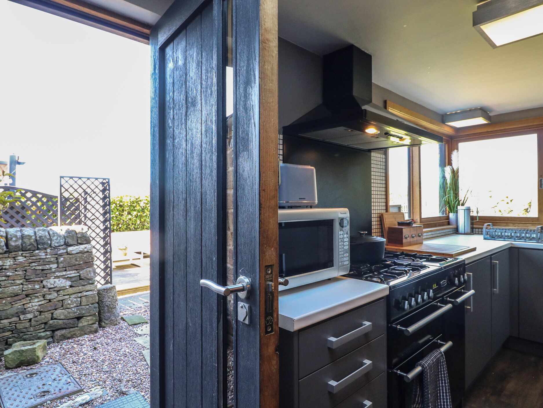 A modern kitchen with a built-in microwave, stove, and oven, featuring a stone wall and a view of the outdoors.