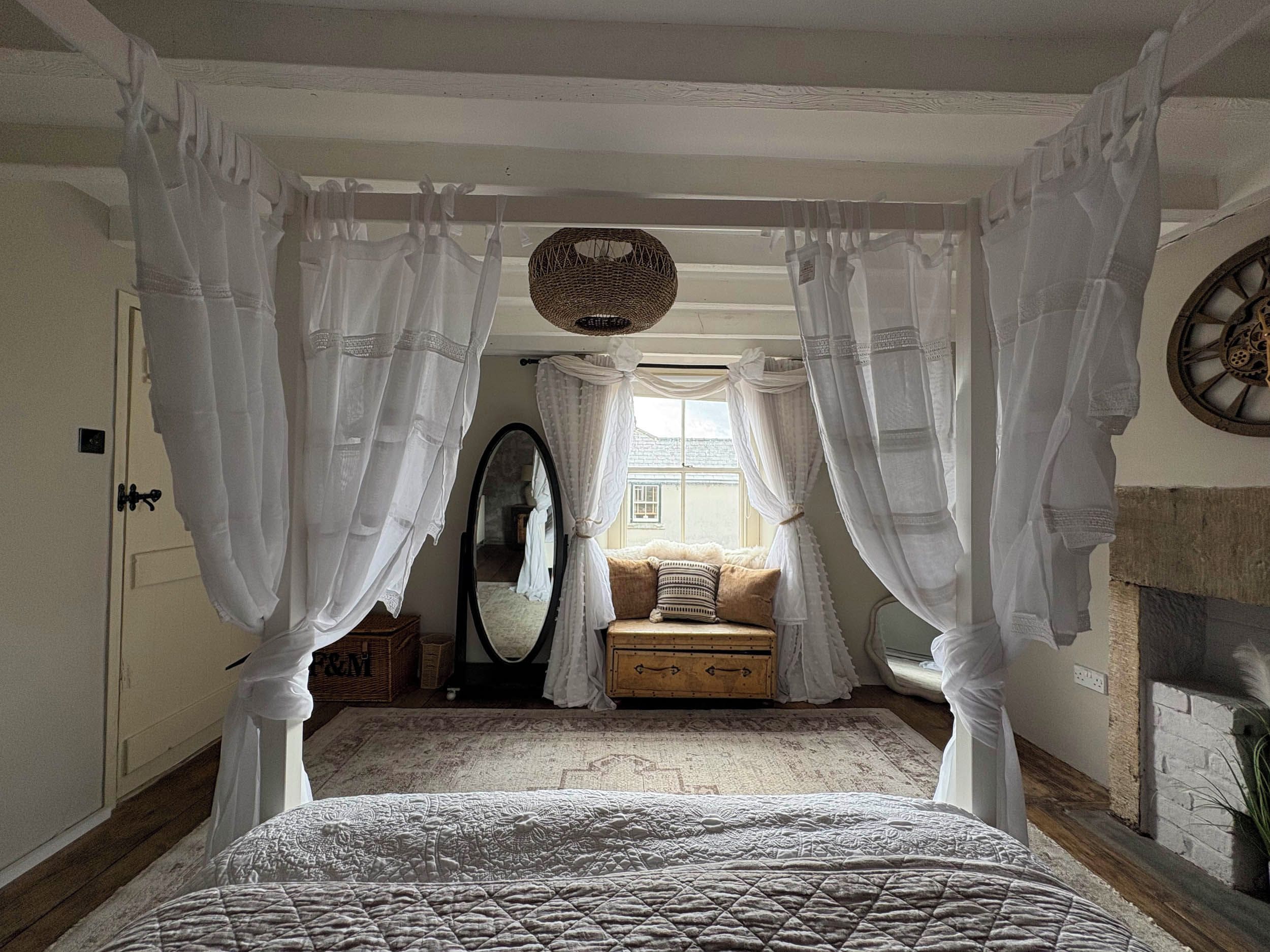 A bedroom with a four-poster bed, a mirror, a sofa, and a fireplace.