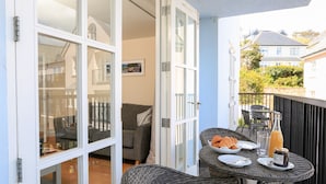 A balcony with wicker furniture, a table with plates, a bottle, and a jar. - 12 Combehaven (Salcombe)