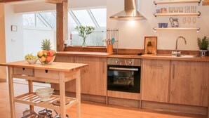 Une cuisine moderne avec des armoires en bois, une hotte de cuisinière en acier inoxydable, un four encastré, un évier et un panier à fruits posé sur le comptoir.
