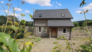 Une maison en bois à deux étages, avec une allée gravillonnée et une clôture en bois en arrière-plan.