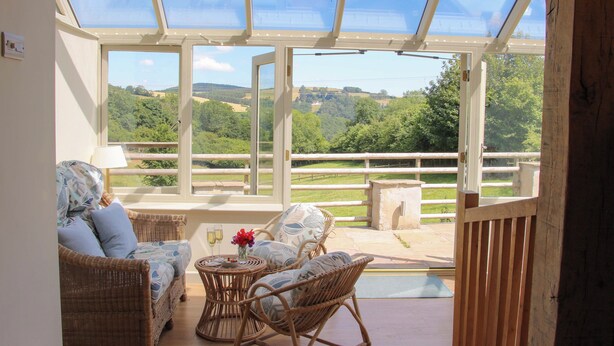 Une véranda meublée de mobilier en osier, offrant une vue sur un paysage verdoyant.