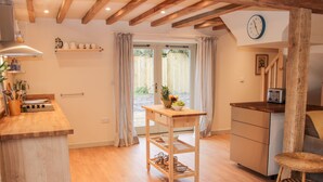 Une cuisine avec des poutres en bois, une table en bois, une chaise en osier et une horloge au mur.