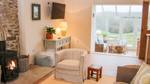 Un salon chaleureux avec une cheminée, un fauteuil confortable, un canapé et un coin repas avec des meubles en osier.