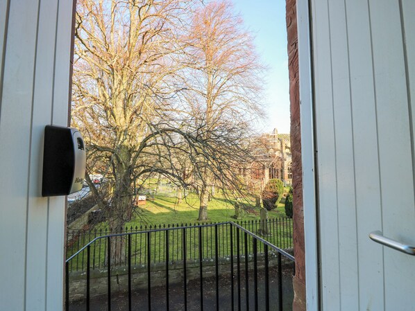 A view through a door with a metal gate leading to a grassy area with trees and a building in the background. - Pear Cottage - Priorwood Garden (Melrose)