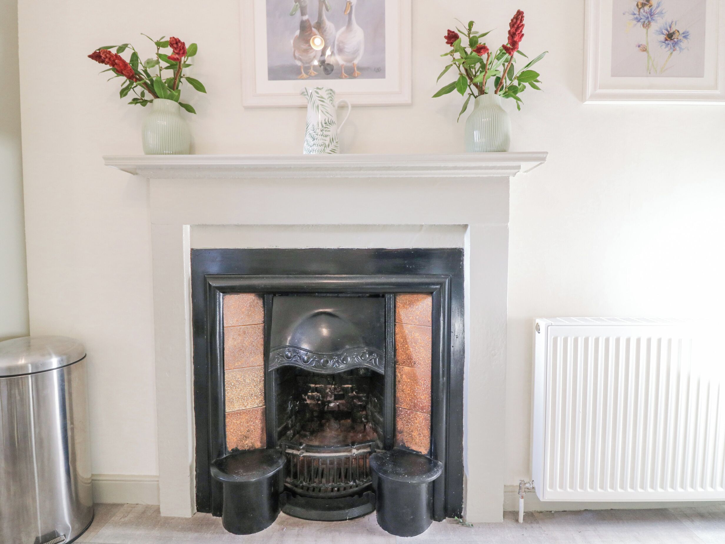 A fireplace with a white mantel, surrounded by framed artwork and vases with flowers.