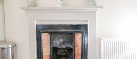 A fireplace with a white mantel, surrounded by framed artwork and vases with flowers.