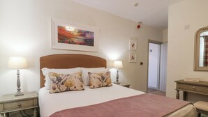Une chambre d’hôtel bien aménagée, avec un grand lit, deux tables de chevet avec des lampes, une tête de lit, un tableau encadré au-dessus du lit et un miroir sur le mur.