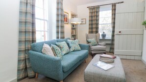 Un salon chaleureux avec un canapé bleu, un pouf assorti et une fenêtre décorée de rideaux à carreaux.