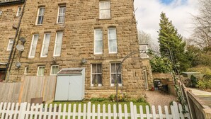 A stone building with multiple windows, a white picket fence, and a small garden area. - The Lanterns (Buxton)