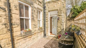 A stone building with a small patio area, a door, and a window with a planter. - The Lanterns (Buxton)