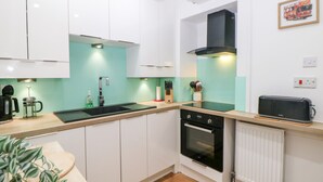 A compact kitchen with white cabinets, a black stove, a sink, and a toaster. - The Lanterns (Buxton)