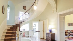 Una amplia escalera con barandilla blanca, piso de madera y una puerta que da a otra habitación.