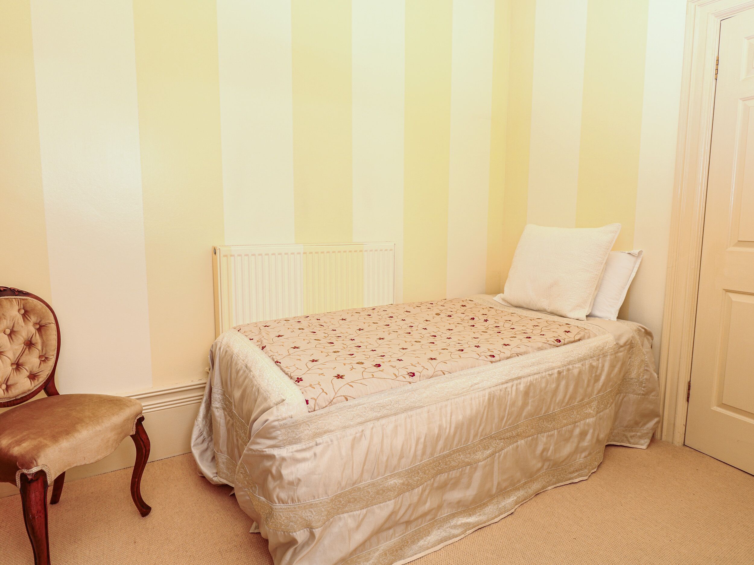 A bedroom with a bed, a chair, a radiator, and a door.