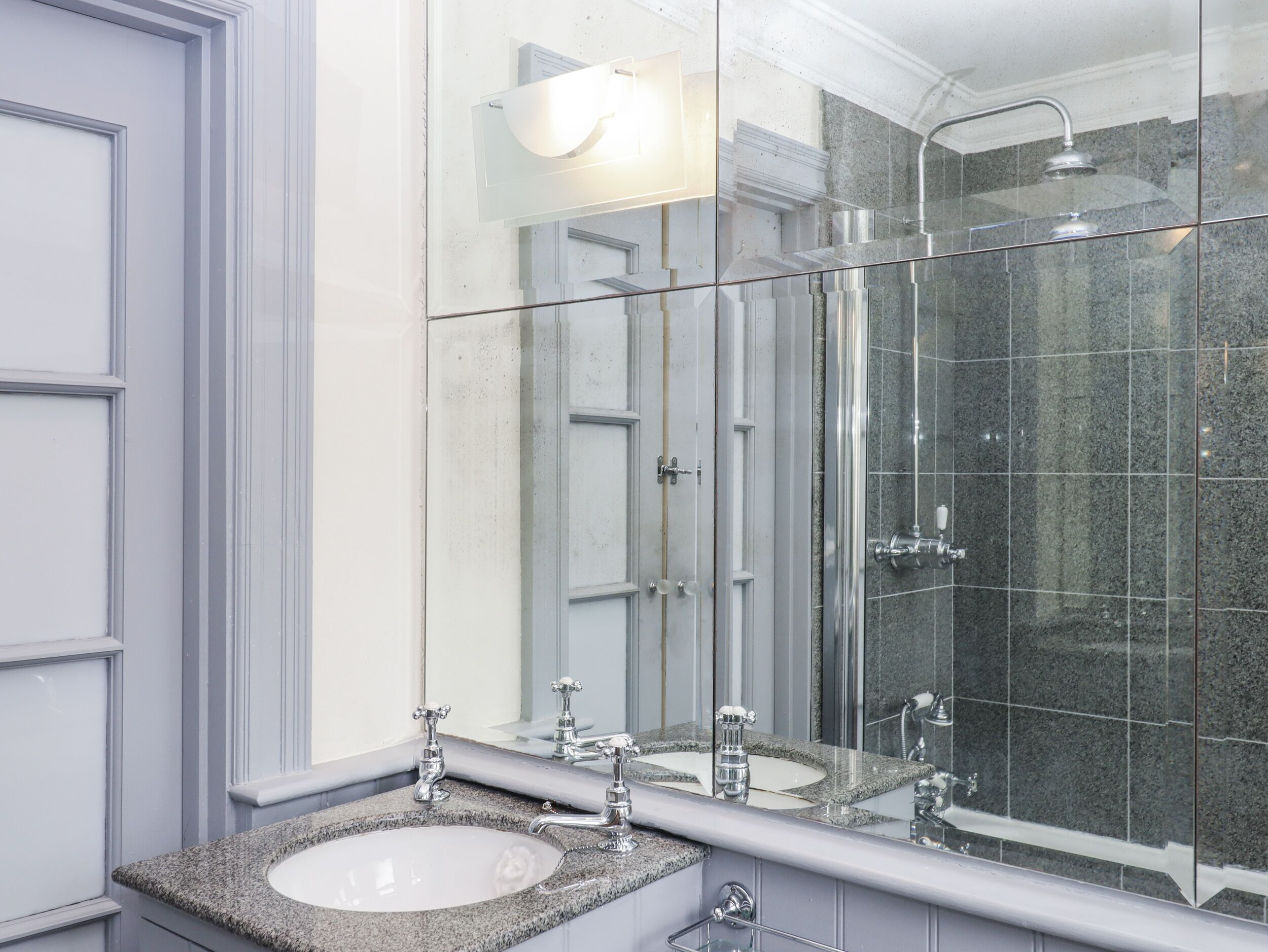 A bathroom with a large mirror, a sink, and a shower.
