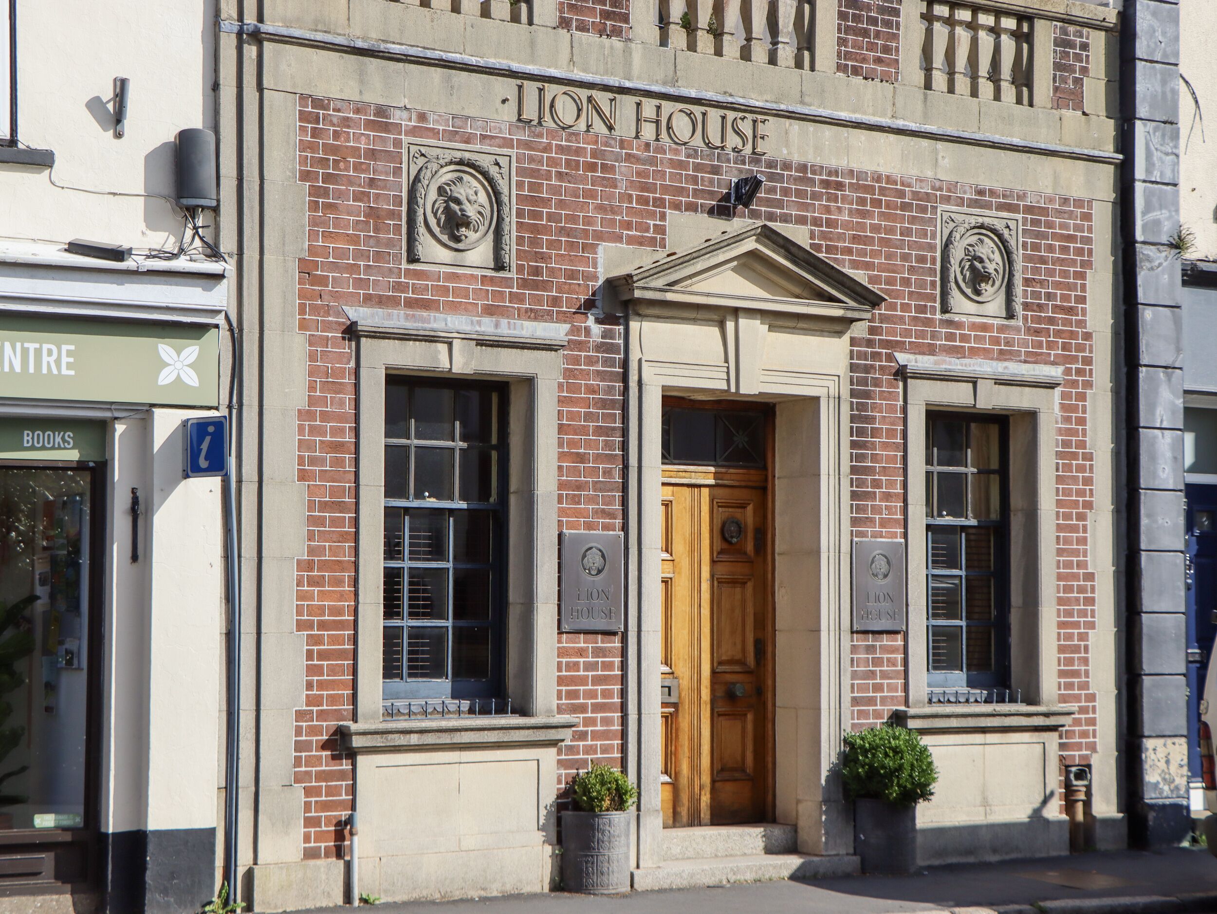 A brick building with a sign reading "Lion House" and a wooden door. There are two windows with shutters, and a small sign on the wall.