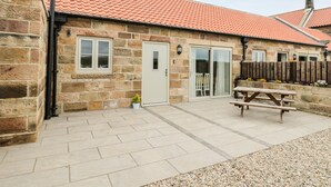 Une maison en pierre avec un toit en tuiles, une porte d’entrée et une porte-fenêtre coulissante donnant sur un patio équipé d’une table de pique-nique.