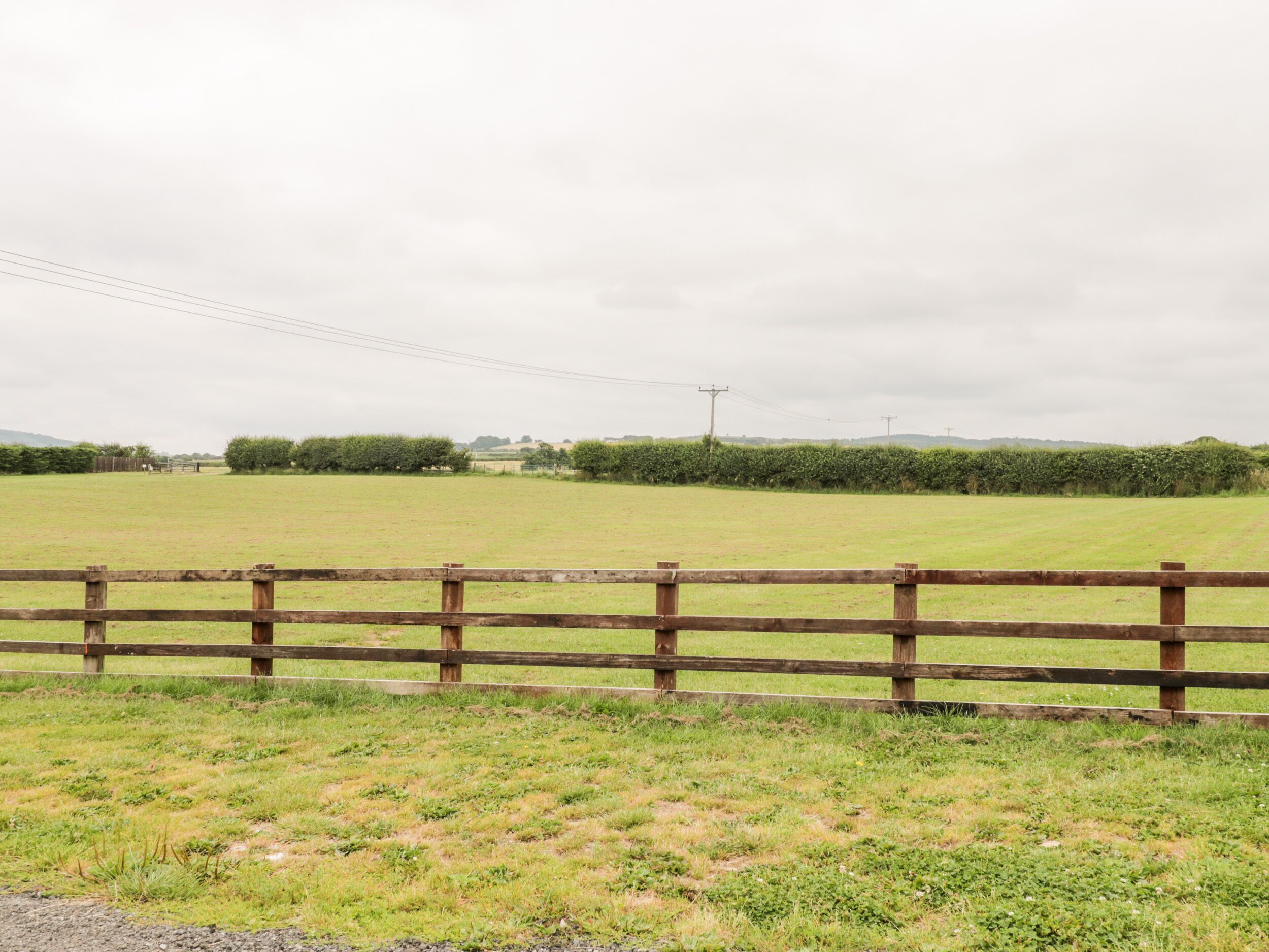 A rural landscape with a wooden fence, open fields, and distant trees.