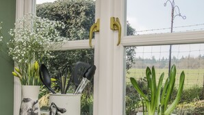 Un rebord de fenêtre dans la cuisine, orné d’ustensiles de cuisine, d’une plante en pot et d’un pot en céramique décoratif orné d’un motif de vache.