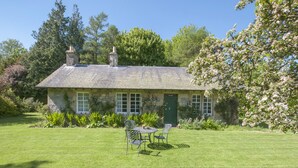 A stone cottage with a green door, a chimney, and a garden with a table and chairs. - Middle Cottage - Tarvit (Cupar)