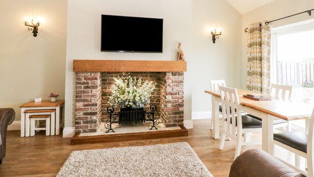 A living room with a fireplace, a television mounted above it, and a dining area with a table and chairs. - Shipswheel Cottage at Broadings Farm (Whitby)