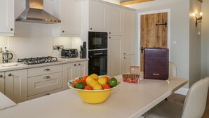 A modern kitchen with white cabinets, a gas stove, a built-in oven, and a wooden door. - Shipswheel Cottage at Broadings Farm (Whitby)