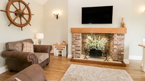 A living room with a fireplace, a mounted TV, and a ship's wheel decoration. - Shipswheel Cottage at Broadings Farm (Whitby)