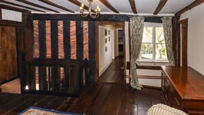 A room with exposed wooden beams, a large window with curtains, a wooden desk, and a patterned rug. - Top Farm House (Oswestry)