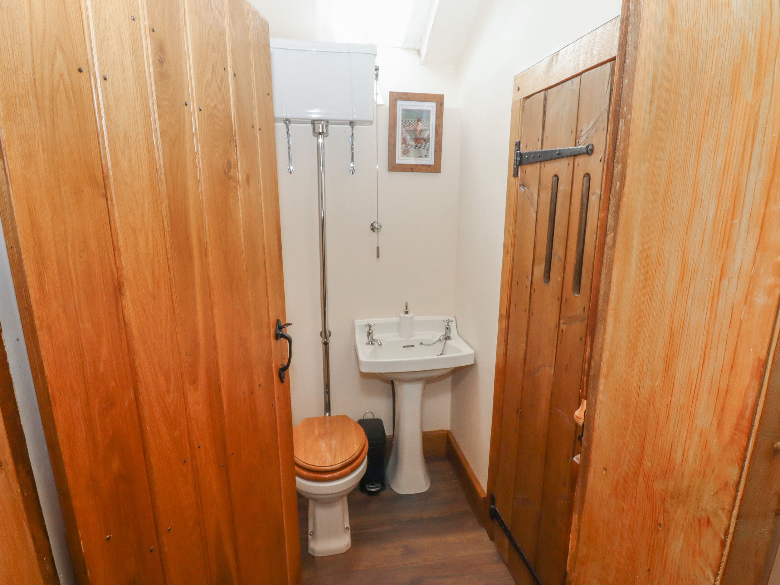 Un baño estrecho con puertas de madera, inodoro blanco, lavabo y ducha.