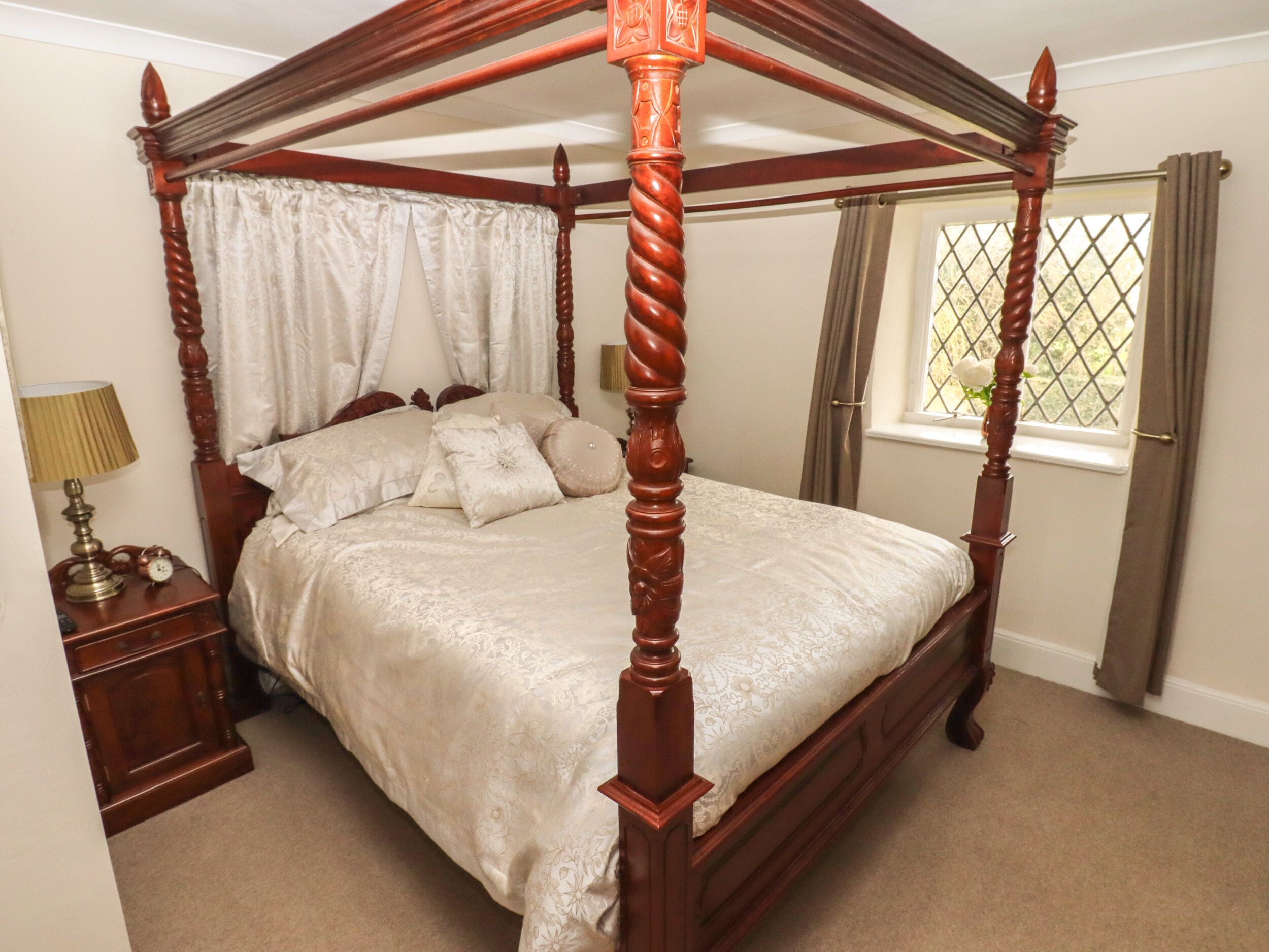 A four-poster bed with a canopy, a bedside table with a lamp, and a window with curtains.