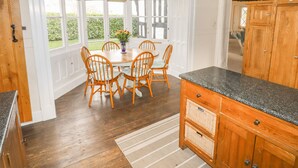 A kitchen with wooden cabinets, a granite countertop, and a dining area with a table and chairs. - Top Farm House (Oswestry)