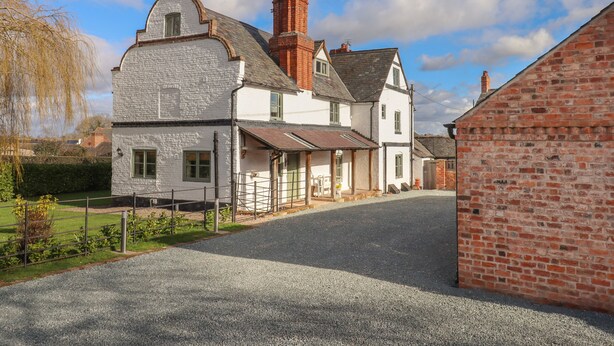 A two-story house with a gravel driveway and a brick wall on the right. - Top Farm House (Oswestry)