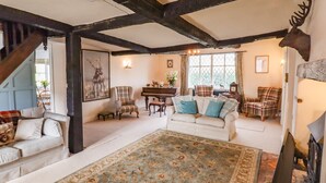 A cozy living room with a large rug, multiple seating areas, a piano, and a deer head decoration. - Top Farm House (Oswestry)