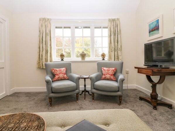 A room with two armchairs, a small table, a television on a wooden stand, and a window with curtains. - West Cottage - Tarvit (Cupar)