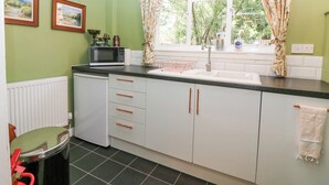 Una cocina con microondas, pileta y alacenas. Hay dos cuadros en la pared y una ventana con cortinas.