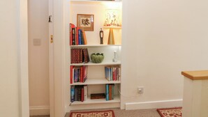 A bookshelf with books, a clock, and a lamp. - Branklyn Garden Cottage (Perth)