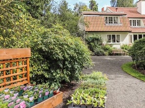A house with a gravel driveway, a wooden fence, and a garden with various plants.