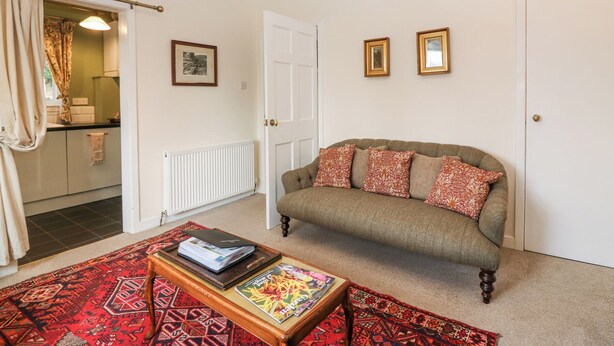 A living room with a sofa, a coffee table, a patterned rug, and a door leading to a kitchen. - Branklyn Garden Cottage (Perth)
