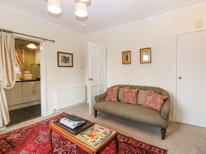 A living room with a sofa, a coffee table, a patterned rug, and a door leading to a kitchen. - Branklyn Garden Cottage (Perth)