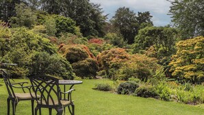 A garden with a table and chairs, surrounded by various trees and shrubs. - Branklyn Garden Cottage (Perth)