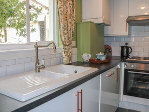 A kitchen with a white sink, stainless steel faucet, and a built-in oven. - Branklyn Garden Cottage (Perth)