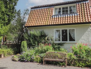 A house with a tiled roof, a front garden with various plants and flowers, and a bench. - Branklyn Garden Cottage (Perth)