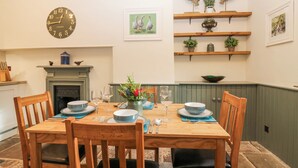 Comedor con una mesa de madera dispuesta para cuatro personas, rodeada de sillas. Un reloj está colgado en la pared sobre la mesa.