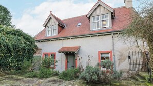 Una casa de dos pisos con techo de tejas rojas, un pequeño porche y un jardín con diversas plantas y un sendero de piedra.